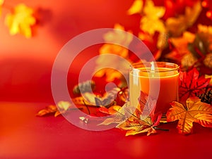 Warm Autumn Ambiance with Lit Candle and Colorful Fall Leaves on a Red Background