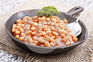 Warm baked beans in tomato sauce served in a cast iron pan