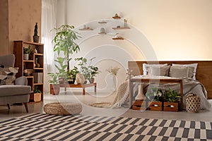 Warm bedroom interior with plants, shelves, striped rug, pouf, b