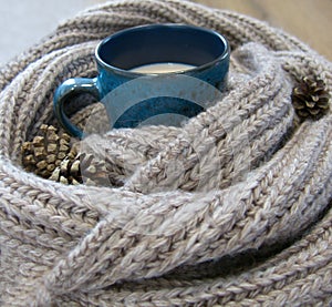 Warm blue mug in the arms of a knitted scarf