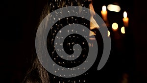 Warm candle light black mysterious background shot of dark hair beautiful young female standing behind the chain curtain