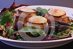 Warm chevre chaud goat cheese baked on rustic bread with green salad and olives. Traditional french dish in close-up