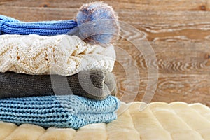 Warm clothing lies in a pile on a fluffy soft rug. Knitted sweaters on a wooden background. Autumn and winter concept