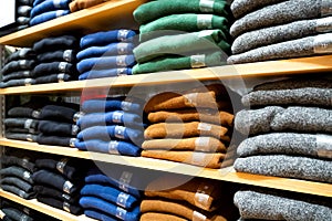 Warm clothing neatly folded on a shelf. A row of colorful jumpers, cardigans, sweatshirts, sweaters, hoodies in the