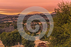 Warm color sunset sky, orange, red, lavender tones, in southern California hills in autumn, oaks in foreground mountains in backgr