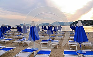 Warm colorful sunset on empty beach with blue chaise longues and calm sea water with old castle in background in Lerici, Liguria,