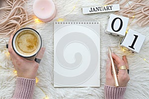 Warm cozy home start new year 1 january on perpetual calendar. Notebook mockup and woman hands holds gold penand cup of