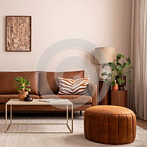 Warm and cozy interior of living room space with brown sofa, pouf, beige carpet, lamp, mock up poster frame, decoration, plant and