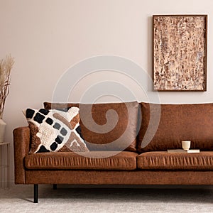 Warm and cozy interior of living room space with mock up poster fame, brown sofa, beige carpet, patterned pillow, modern pouf,