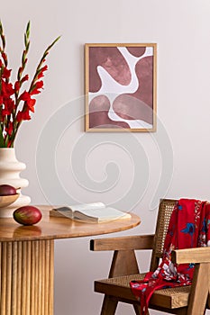 Warm and cozy interior of living room space with mock up poster frame, wooden table, red flowers, kimono, rattan chair, decoration