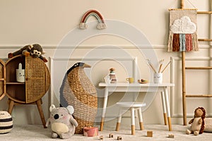 Warm and cozy kids room interior with white desk, stool, animal wicker basket, rattan sideboard, stylish toys, plush monkey, koala