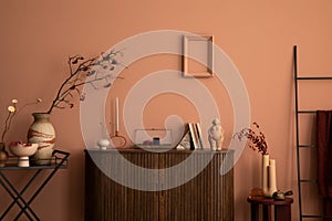 Warm and cozy living room interior with frame, wooden commode, ladder, round coffee table vase with dried flowers, sculpture,