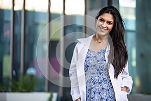 Warm, friendly portrait of a mixed ethnicity brunette female practitioner standing outside of her medical private practice