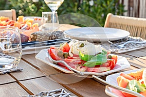 The warm glow of the evening sun enhances an appetizing plate of Caprese salad, complete with creamy Mozzarella, tomatoes, olives