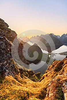 Warm glow over Reinebringen\'s moss-covered rocks with Reinefjorden reflecting Lofoten\'s majesty