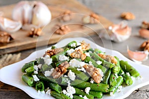 Warm green bean salad. Easy green string beans salad with cottage cheese, peeled walnuts, garlic and spices on a white plate