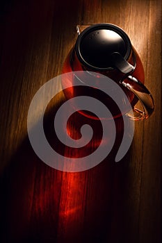 A warm-hued teapot on a wooden surface, steeping tea, casting reflections and shadows