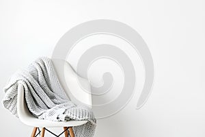 Warm knit grey blanket on a chair on white wall background