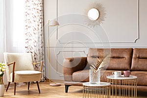 Warm living room interior with a leather sofa, armchair, lamp and coffee tables with a vase