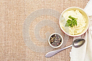 Warm mashed potatoes in a ceramic bowl with fresh parsley and dry pepper mix. On a linen cloth background, copy space, top view,