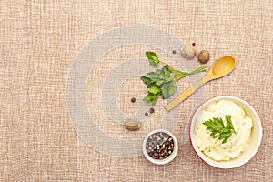 Warm mashed potatoes in a ceramic bowl with fresh parsley and dry spices. On a linen cloth background