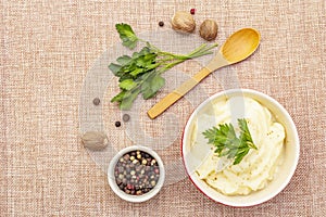 Warm mashed potatoes in a ceramic bowl with fresh parsley and dry spices. On a linen cloth background