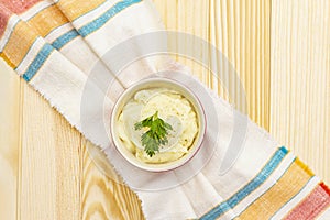 Warm mashed potatoes in a ceramic bowl with fresh parsley. On a vintage linen napkin on a stone background, top view, copy space,