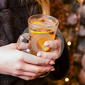 Warm mulled wine in female hands, Christmas decorations on the background
