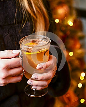 Warm mulled wine in female hands, Christmas decorations on the background
