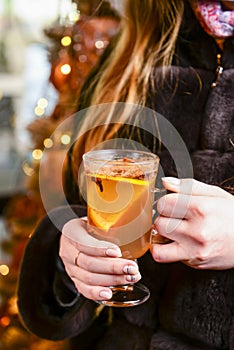 Warm mulled wine in female hands, Christmas decorations on the background