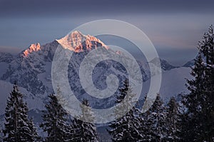 Warm orange sunset light painting the top of snow-covered mountains in winter time