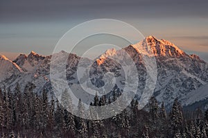 Warm orange sunset light painting the top of snow-covered mountains in winter time