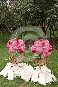 Warm pink blankets rolled up in the form of roses in a large basket for guests at an outdoor wedding party. Individual dance white