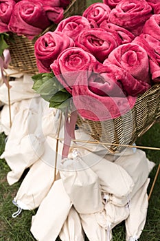 Warm pink blankets rolled up in the form of roses in a large basket for guests at an outdoor wedding party. Individual dance white