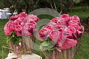 Warm pink blankets rolled up in the form of roses in a large basket for guests at an outdoor wedding party. Individual dance white