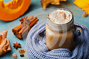 Warm pumpkin spiced latte or coffee in cup decorated knitted scarf on turquoise vintage background. Autumn, fall or winter drink.