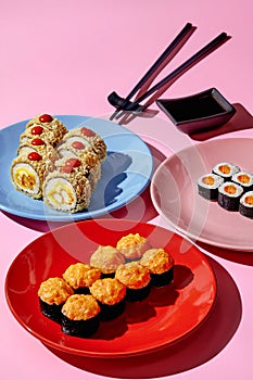 Warm rolls with tempura shrimp, maki sushi with masago and salmon on colorful plates