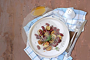Warm salad of grilled Jerusalem artichoke and boiled red beans with olive oil and vinegar dressing on a white clay plate