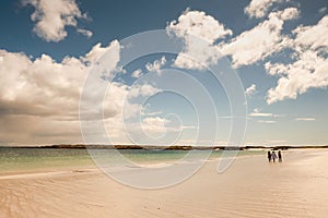 Warm sandy beach of Gurteen bay, county Galway, Ireland. Three women walking on the sand. Warm sunny day. Cloudy sky. Irish nature