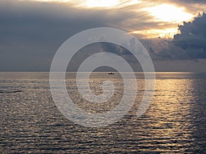 Warm sea sunset with little fishing boat on the water . Giants cumulonimbus clouds in the sky and sun rays through . Tuscany, Ital