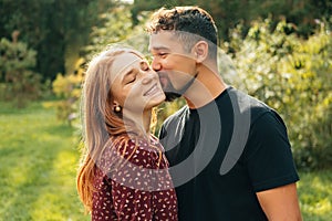 Warm shot of a beautiful happy couple where man kisses his woman in park.