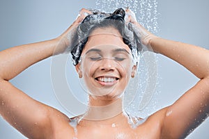 A warm shower keeps the stress away. Shot of a young woman washing her hair in the shower against a grey background.