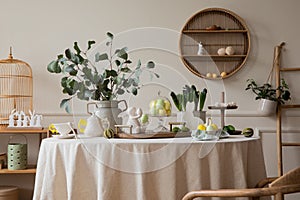 Warm and spring dining room interior with easter accessories, shelf on wall, round table, vase with green leaves, colorful eggs,