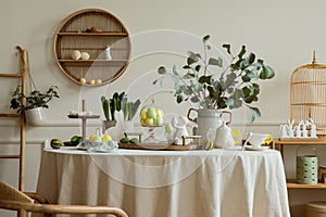 Warm and spring dining room interior with easter accessories, shelf on wall, round table, vase with green leaves, colorful eggs,