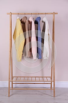 Warm sweaters hanging on wooden rack near pink wall