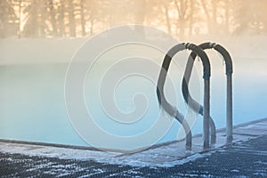 Warm swimming pool hand rail in frosty weather, outdoor, soft focus on stainless steel stair railing covered with ice, close up