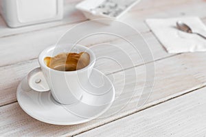 Warm tasty rich italian black espresso coffee cup in white mug on vintage biege wooden rerto style table at cafe or restaurant.