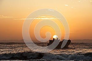 Warm toned image of a sunset with a ship wreck and a flock of sea birds silhouetted against the sunset
