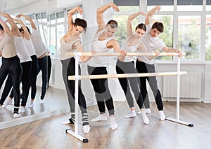 Warm-up sessions, young women and men doing ballet exercise standing in 3rd position in hall with ballet bar photo