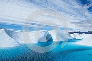 Warm weather melting the ice of the Matanuska Glacier into a large blue pool. An ice cave cuts into the ice, also flooded with the